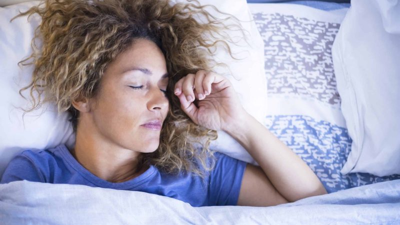 Relax and sleep concept with beautiful caucasian woman sleeping in the morning light at home or hotel - relaxed people in the bed - white pillows and sheet - new day life concept