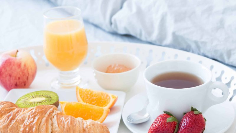 Close-up of tray with tasty breakfast on a bed.