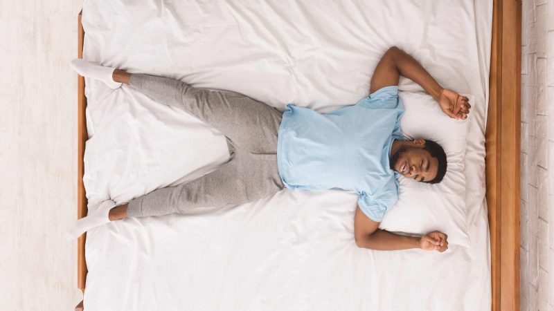 Young african-american man sleeping in bed alone, top view